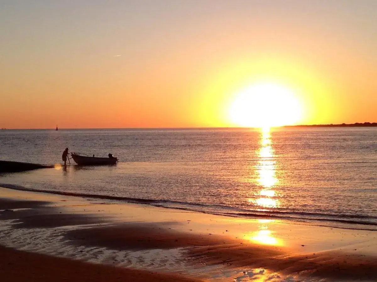 Atardecer en Sanlúcar de Barrameda. Un pescador empuja su barca en la orilla mientras el sol se pone. Imprescindible que ver en Sanlúcar de Barrameda.