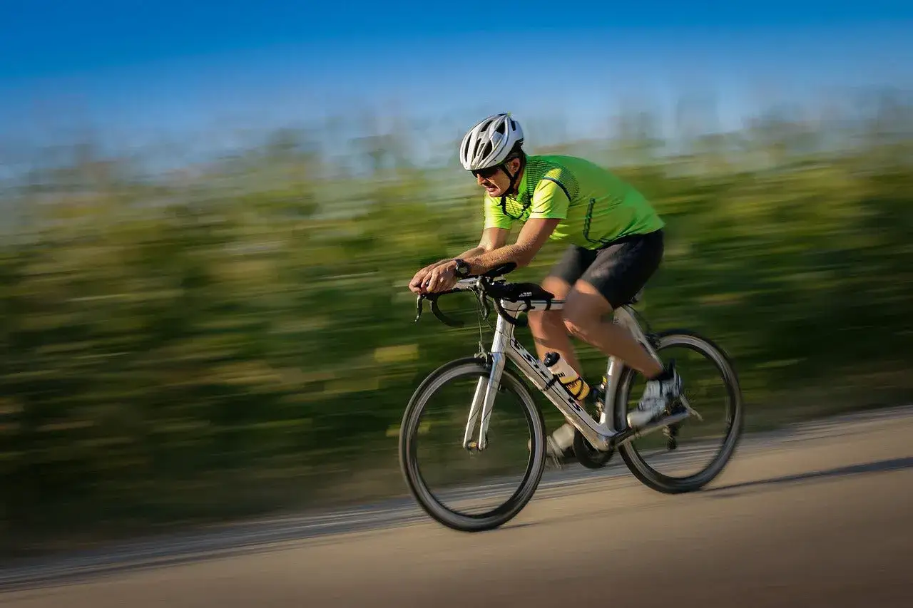 A cyclist in a green shirt and white helmet speeds along a road, blurring the green fields beside them.