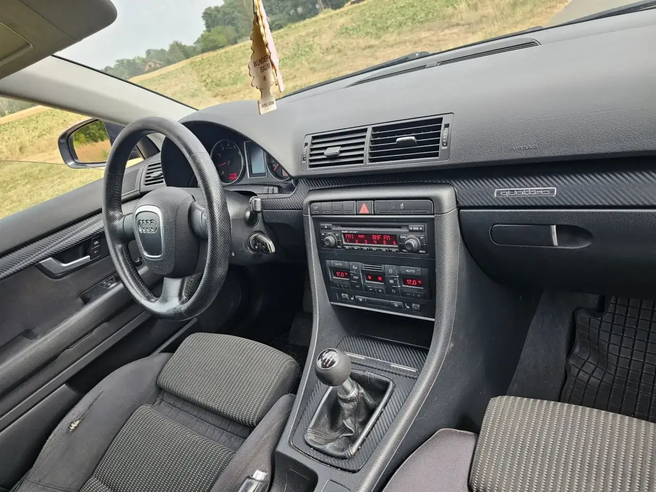 Wnętrze Audi B7 z widoczną kierownicą, deską rozdzielczą z radiem i nawiewami, a także dźwignią zmiany biegów.