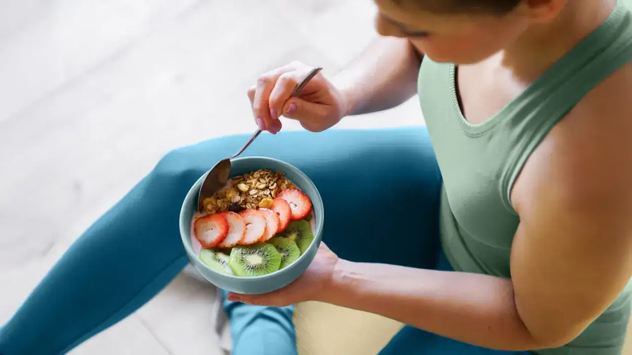 Femme mange un bol de granola, fraises et kiwis. Parfait pour la musculation sèche, ce repas est riche en glucides sains.