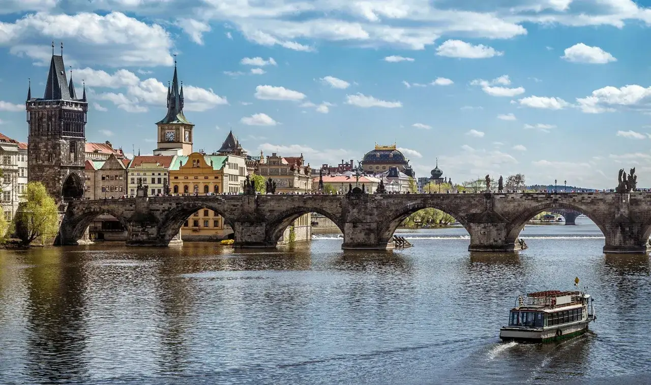 Słynny most Karola w Czechach, z łodzią na Wełtawie i zabytkową panoramą miasta w tle.