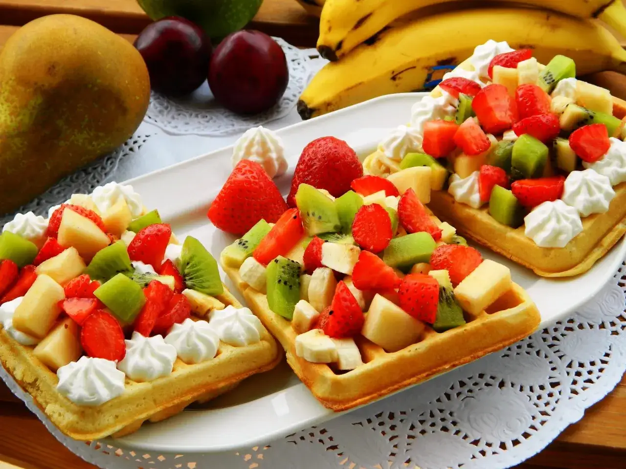 Gofry jak z budki, obficie udekorowane bitą śmietaną i świeżymi owocami: truskawkami, kiwi i bananami.