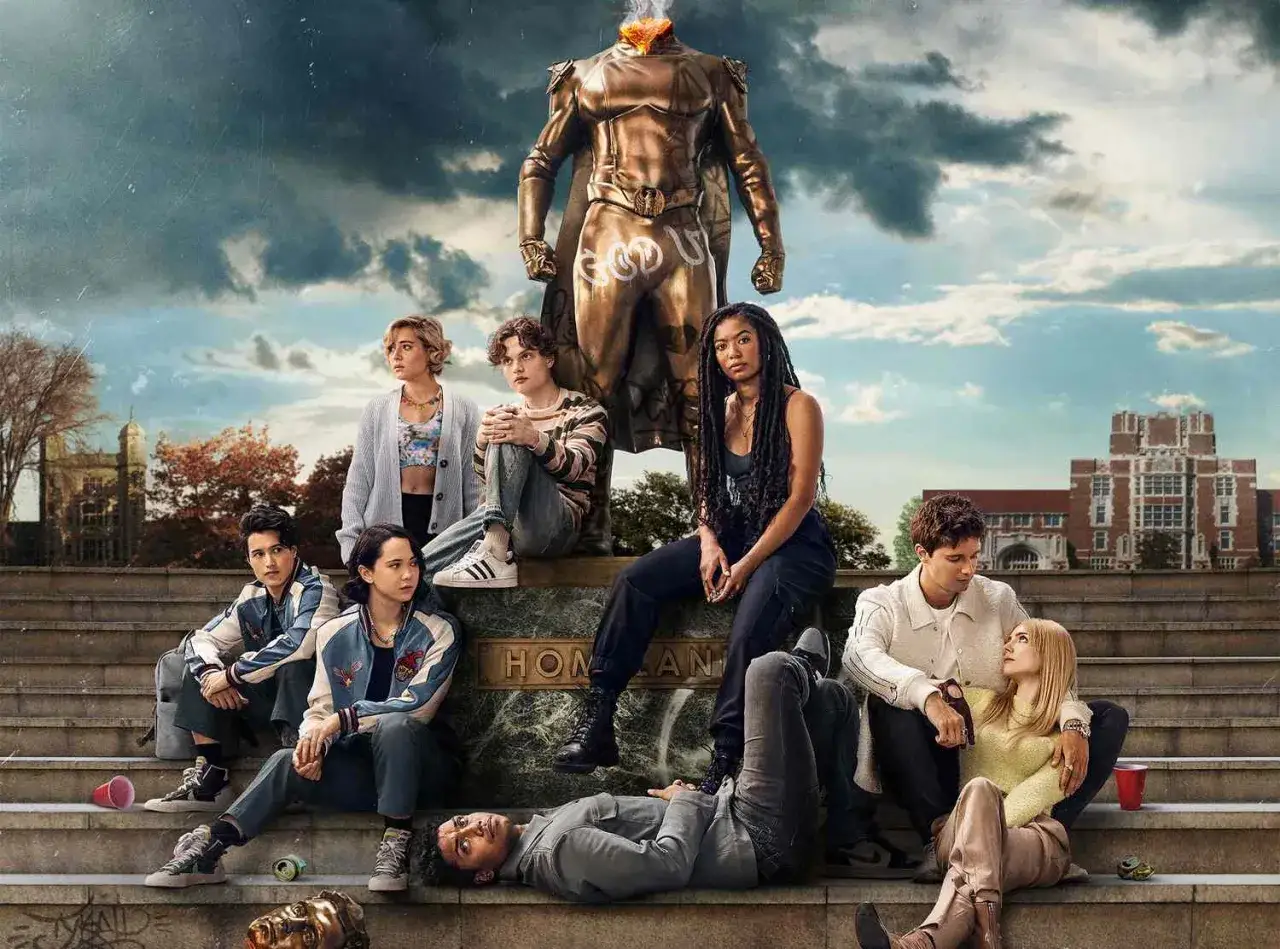 Le casting de **gen v saison 3** pose devant une statue. Des étudiants sont assis sur des marches, certains se tenant la main, d'autres regardant ailleurs.