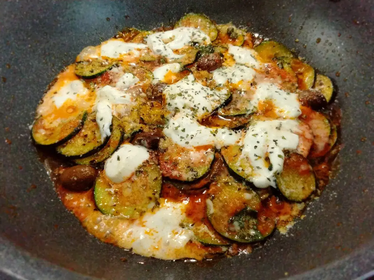 Zucchine alla pizzaiola cotte in padella, con pomodoro, mozzarella filante e olive nere. Un piatto saporito e invitante.