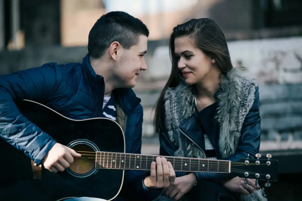 Chłopak gra na gitarze dla dziewczyny, patrzą na siebie z uśmiechem. To może być jeden z pięknych etapów związku nastolatków.