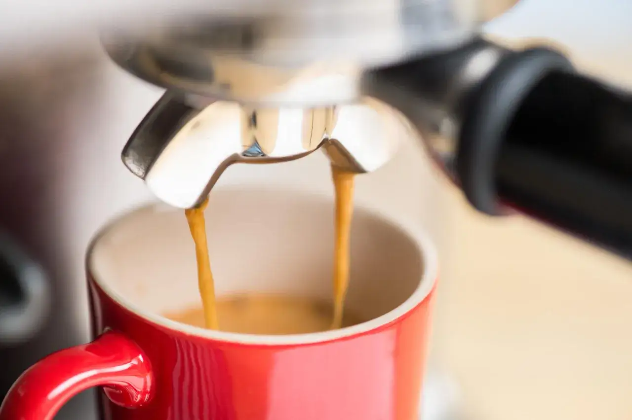 Gorące espresso doppio leje się z ekspresu do czerwonej filiżanki, tworząc idealną cremę.