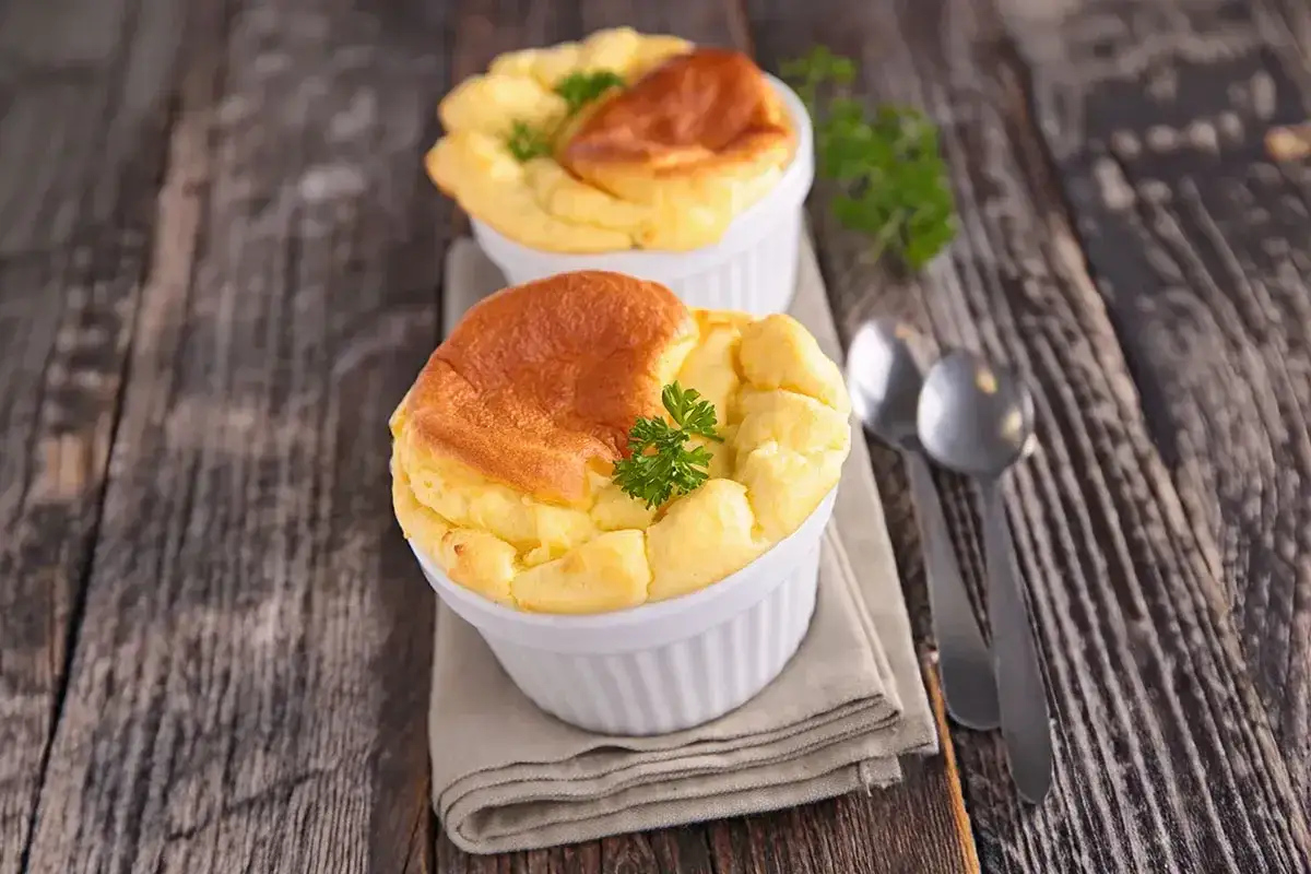 Deux soufflés au fromage dorés et aériens, ornés d'une touche de persil, prêts à être dégustés sur une table en bois rustique.