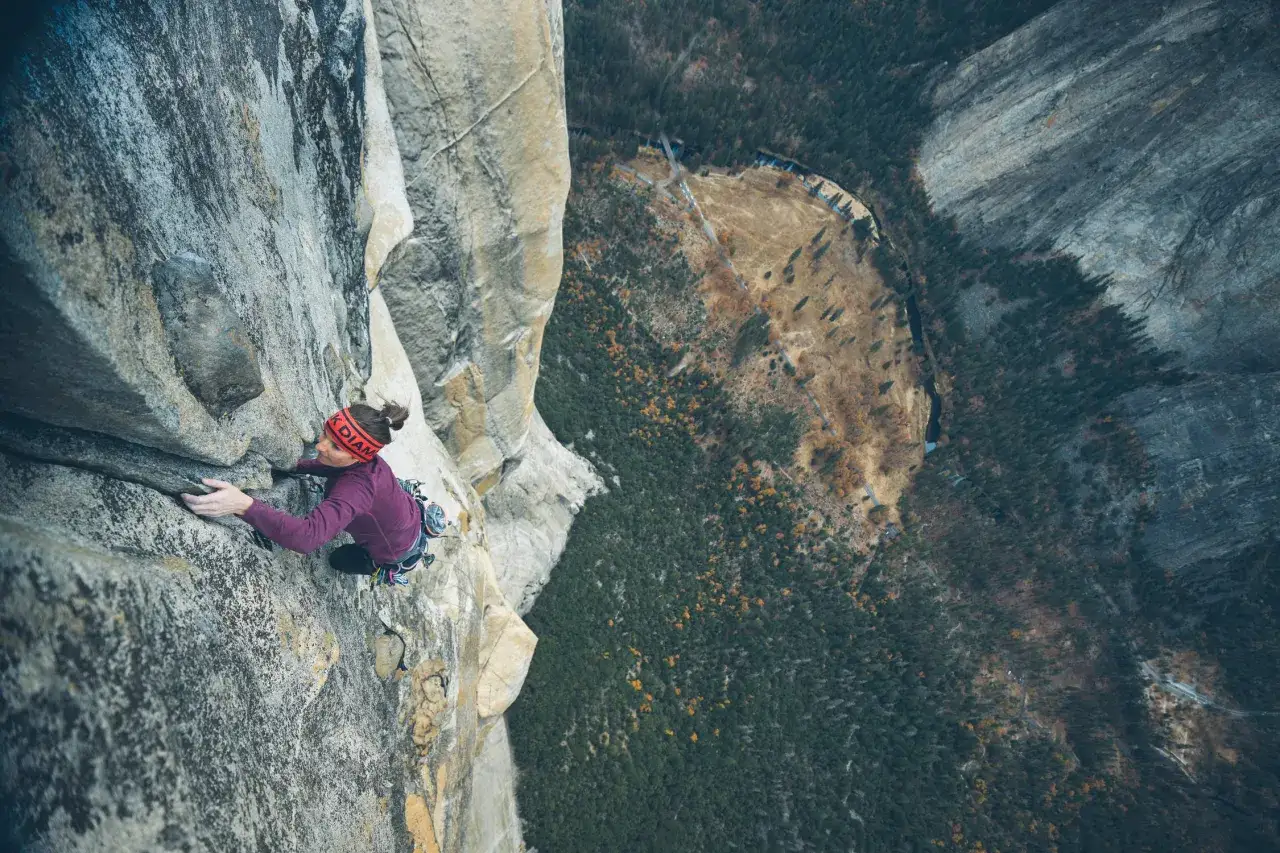 Babsi Zangerl klettert eine steile Felswand empor, mit einem atemberaubenden Blick auf einen bewaldeten Canyon.