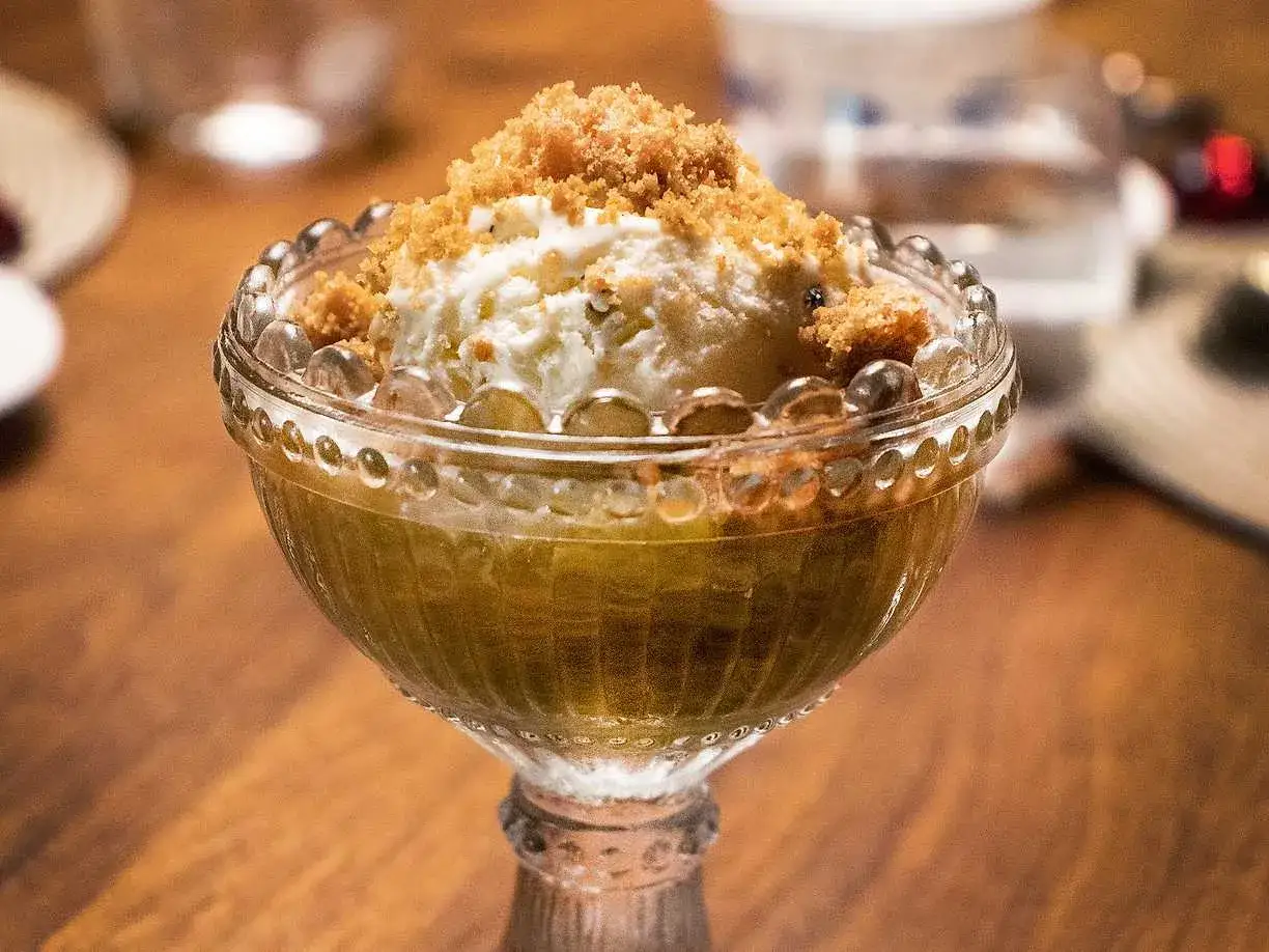 En dessertskål med rabarberkompott och kardemumma, toppad med vaniljglass och smuldeg.