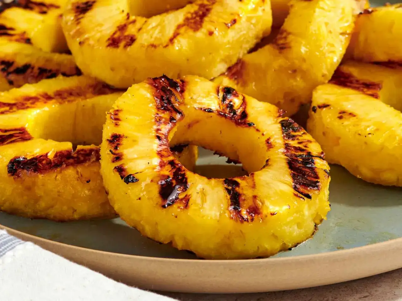 Tranches d'ananas grillées, caramélisées et marquées par le barbecue, servies sur une assiette bleue.