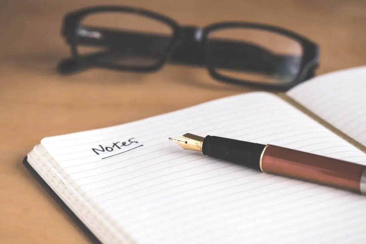Notes na kartce, pióro i okulary. Ktoś tworzy tekst, jak ghostwriter.