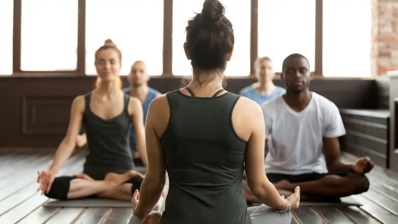 En grupp människor sitter i lotusställning under en yogaklass. De utövar yoga, en andlig praktik som kan liknas vid en religion för vissa.