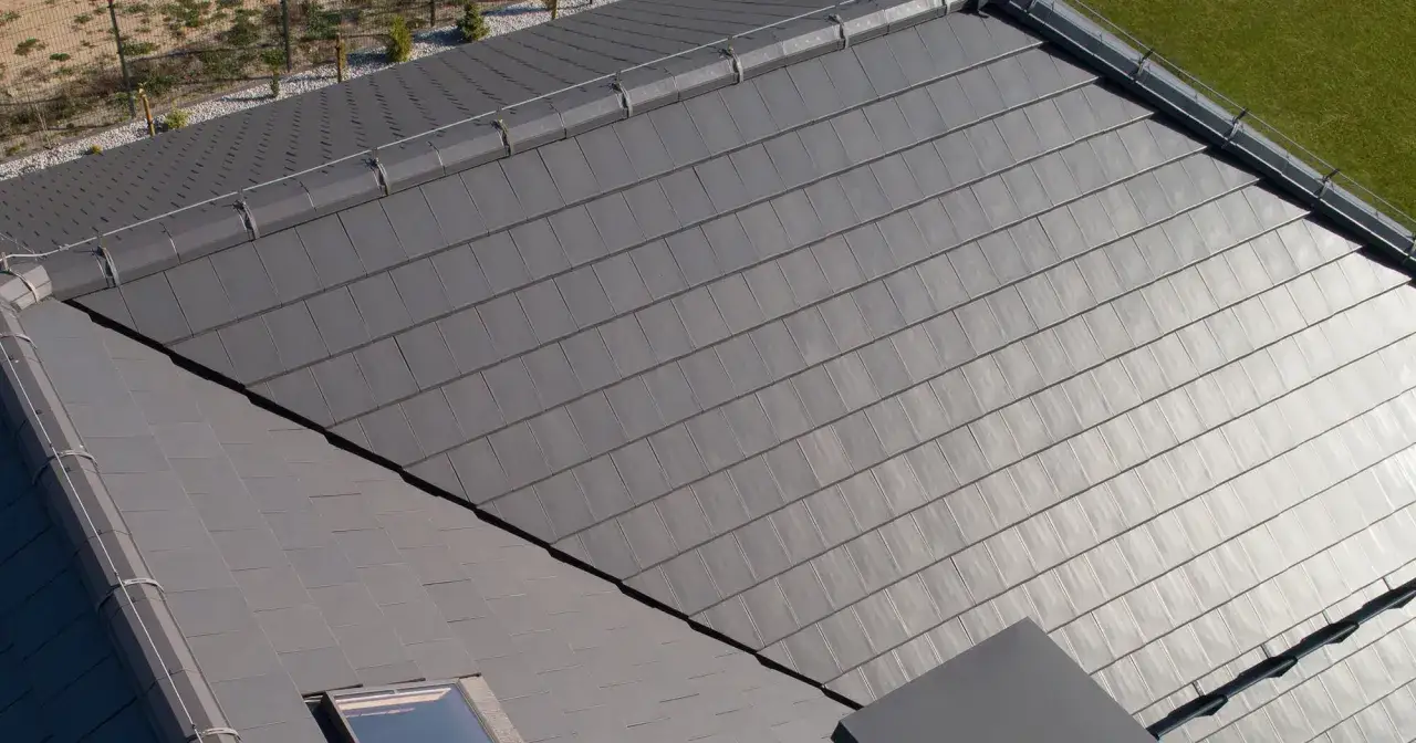 Nowoczesny dach pokryty ciemnoszarą angobą ceramiczną, z widocznym oknem dachowym i fragmentem zielonego trawnika.