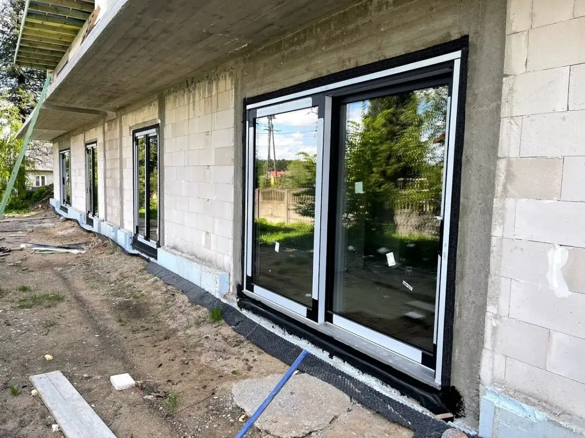 Nowe okna z czarnymi ramami zamontowane w ścianie z bloczków. Wokół okien zastosowano taśmę EPDM do okien, zapewniającą szczelność.