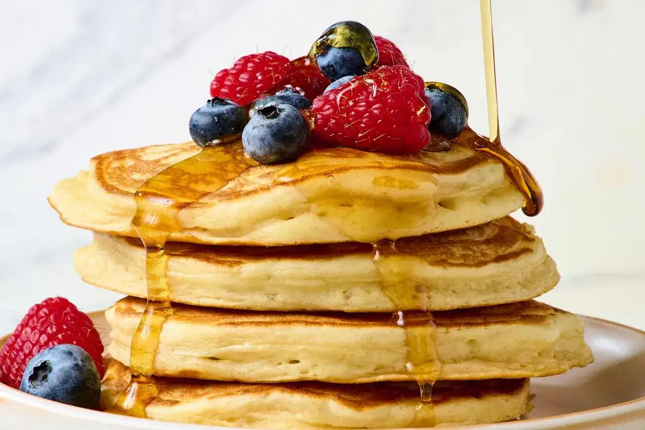 Stapel fluffiger protein pfannkuchen, &uuml;bergossen mit Sirup und garniert mit frischen Beeren.