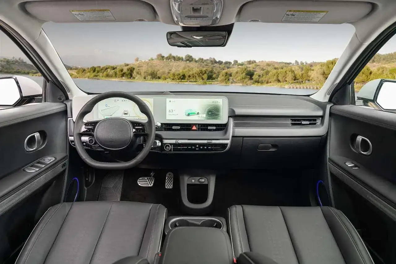 Wnętrze Hyundai Ioniq 5 z widokiem na jezioro i wzgórza. Nowoczesna deska rozdzielcza z dwoma ekranami i minimalistycznym designem.