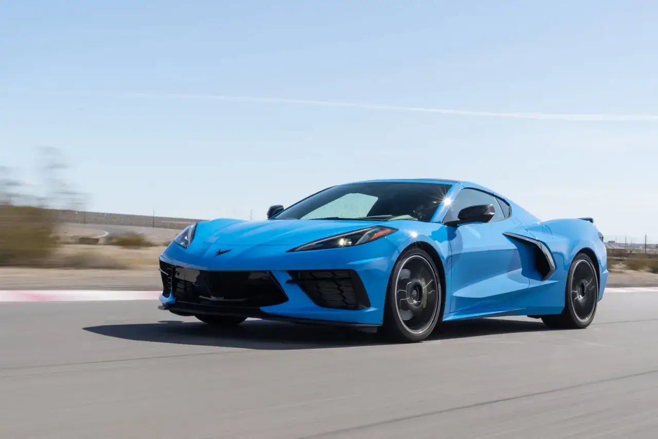 Błękitny Chevrolet Corvette Stingray pędzi po torze wyścigowym, błyszcząc w słońcu.