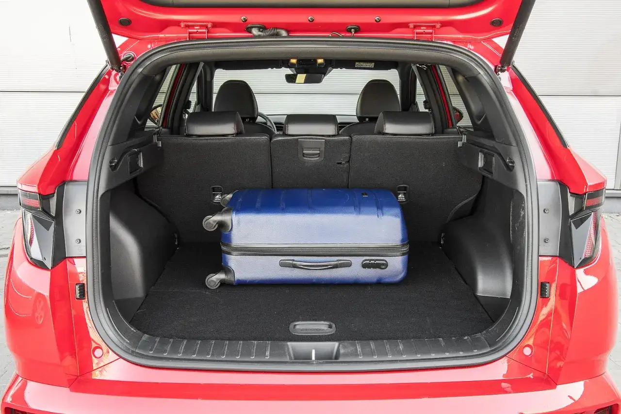 Bagażnik czerwonego Hyundai Tucson, z widocznymi wymiarami wnętrza, mieści niebieską walizkę.