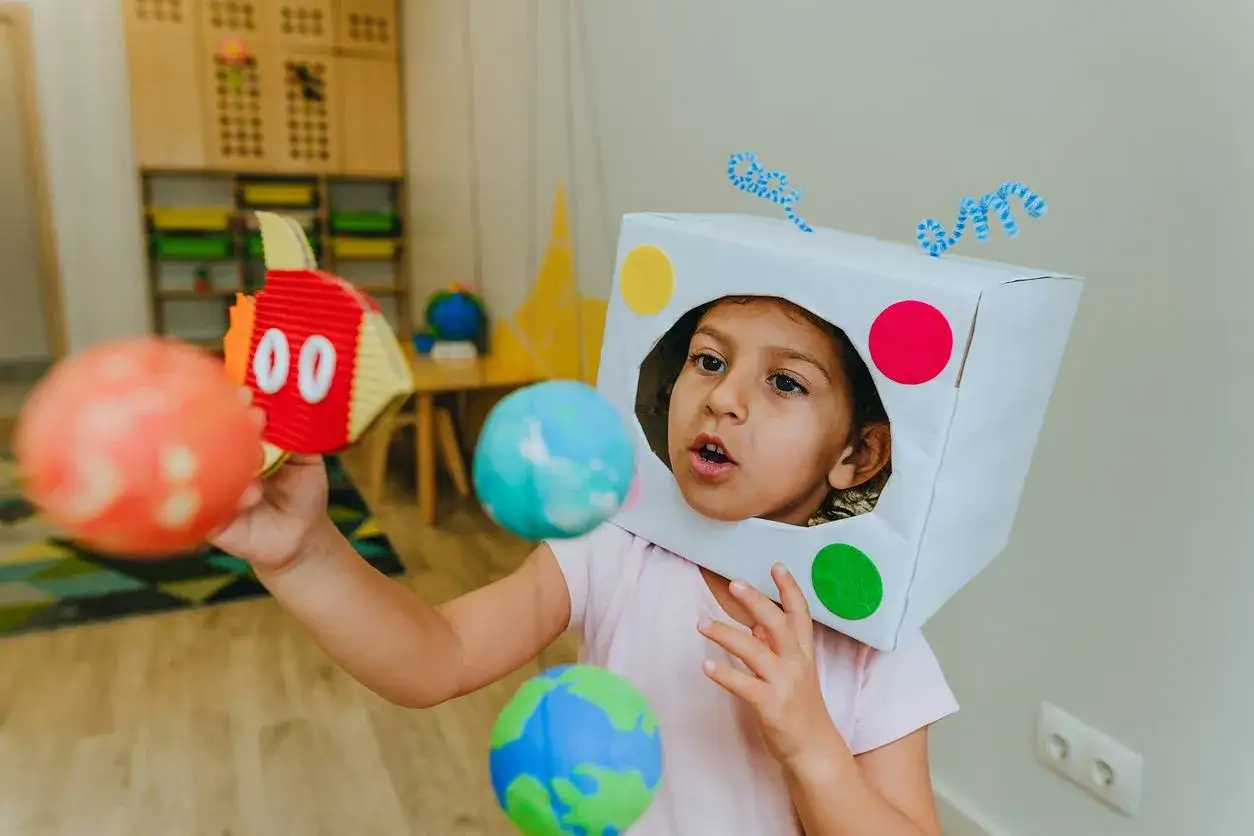 Dziecko w stroju dziadka-robota z planety bawi się kulami-planetami.