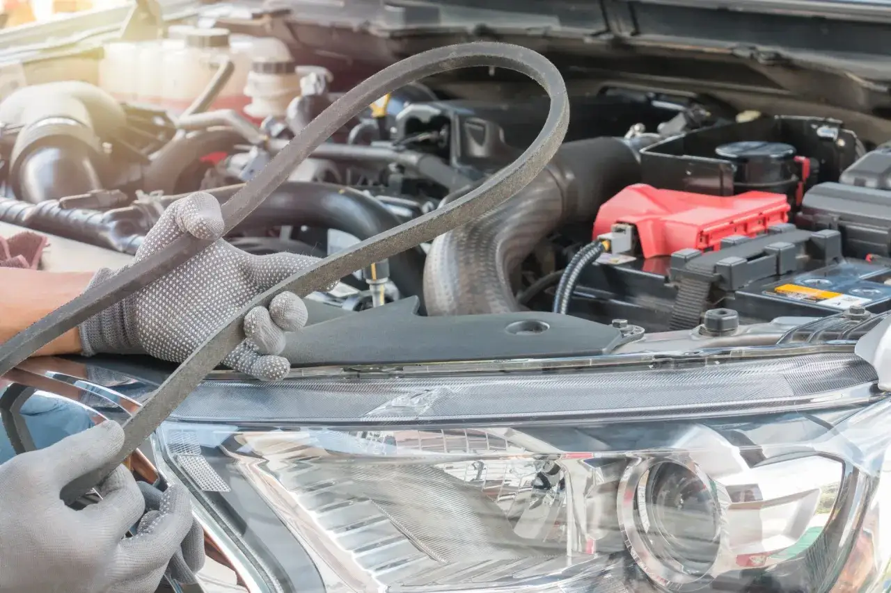 Mechanik w rękawiczkach trzyma pasek klinowy, który mógł być przyczyną problemów z ładowaniem akumulatora.