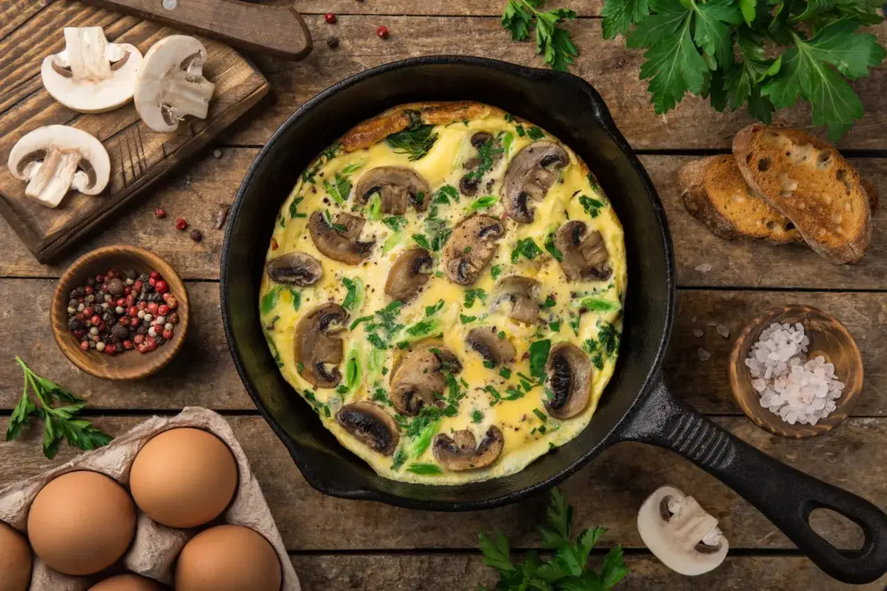 Omelette aux champignons et persil dans une poêle en fonte, accompagnée d'œufs, de pain grillé et d'épices. Un délice de champignon oeuf.