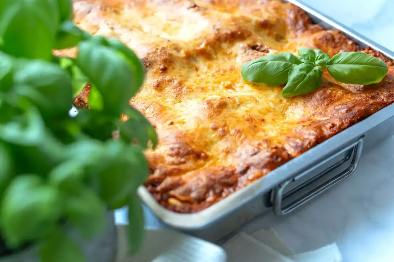 Frisch gebackene italienische Lasagne in einer Metallform, garniert mit Basilikum.