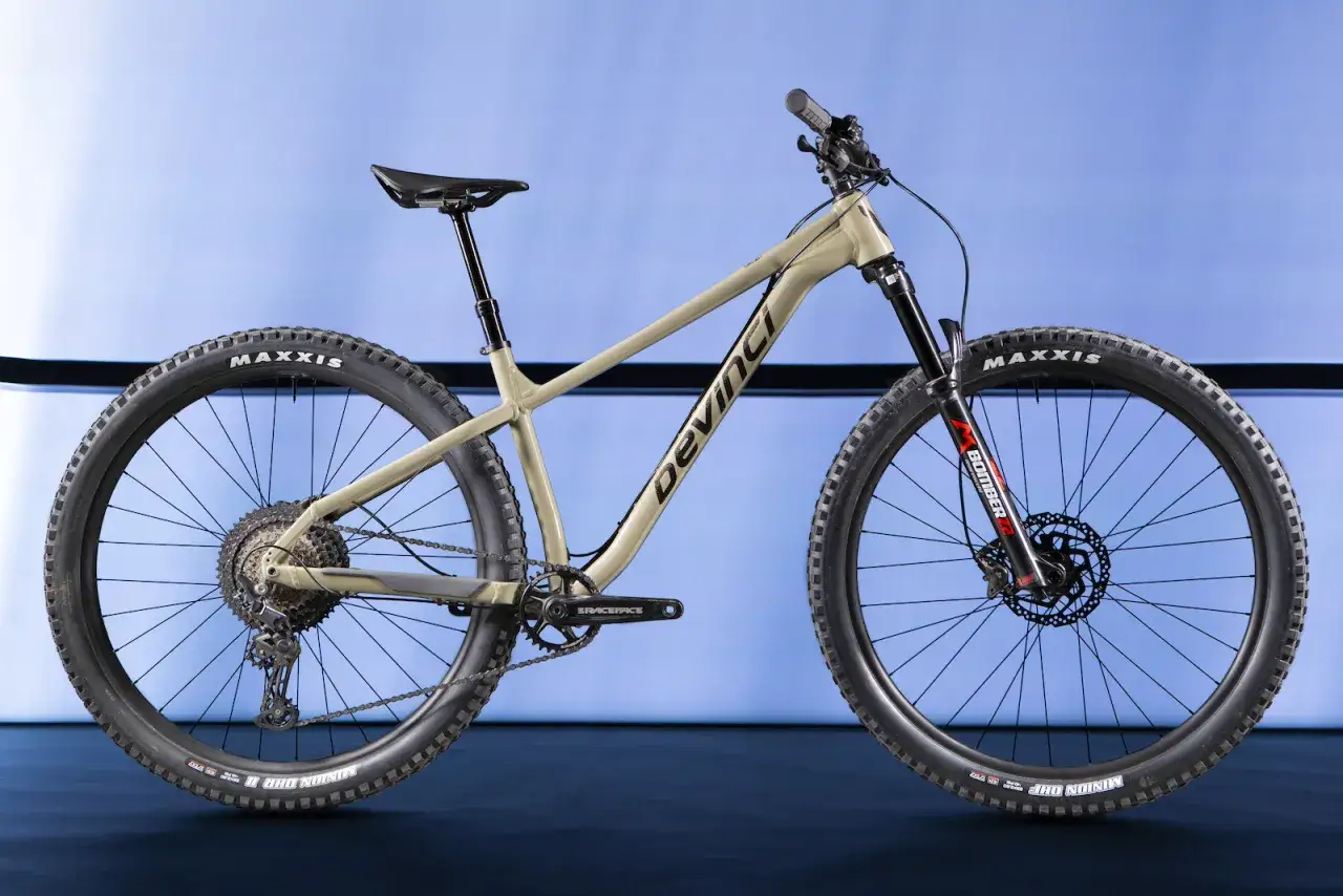 A tan Devinci Kobain hardtail mountain bike with Maxxis tires and a Marzocchi Bomber fork, ready for any trail.