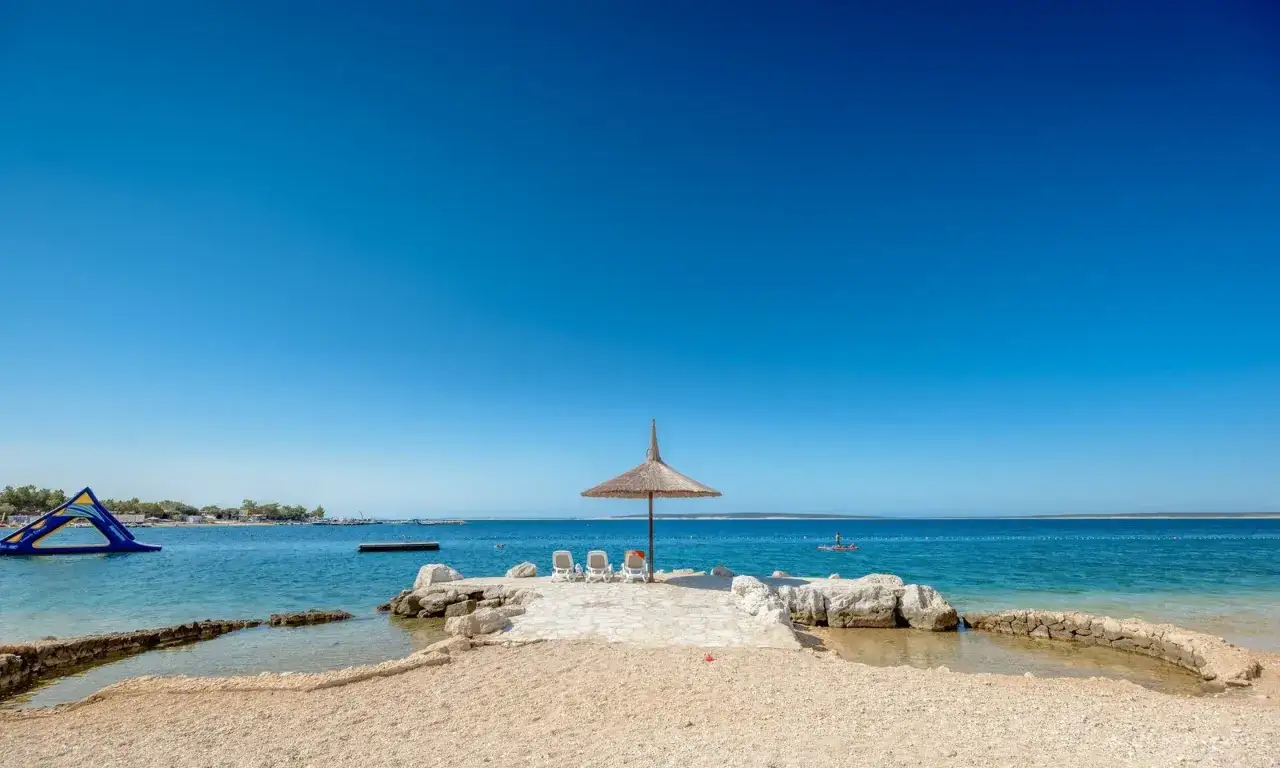 Słoneczny dzień na plaży w Simuni camping. Leżaki pod parasolem, dmuchany plac zabaw w wodzie i błękitne morze.