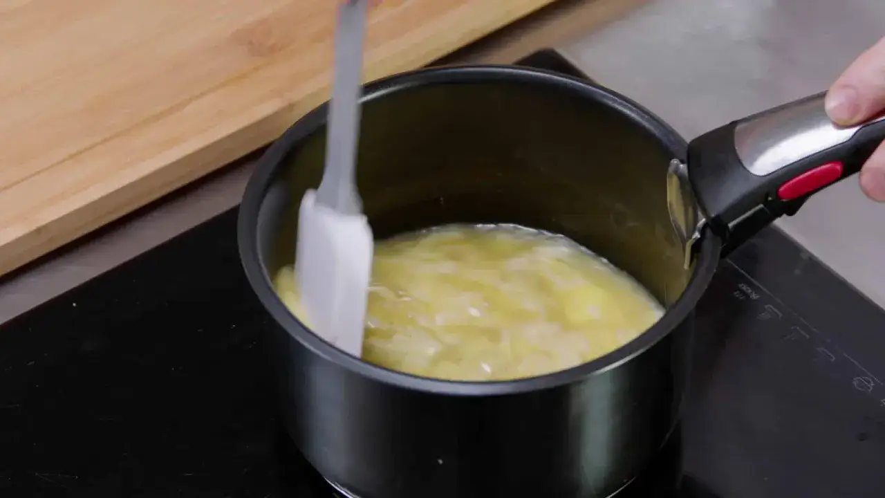 Une spatule mélange des œufs brouillés dans une casserole sur une plaque de cuisson.