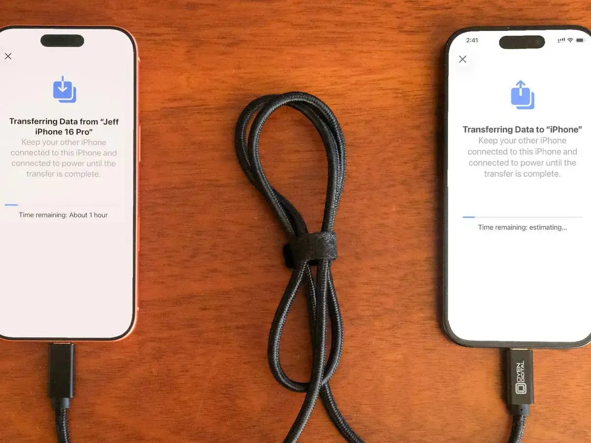 Dwa iPhone'y połączone kablem, jeden przesyła dane na drugi. Proces pokazuje, jak przenieść zdjęcia z telefonu na telefon.