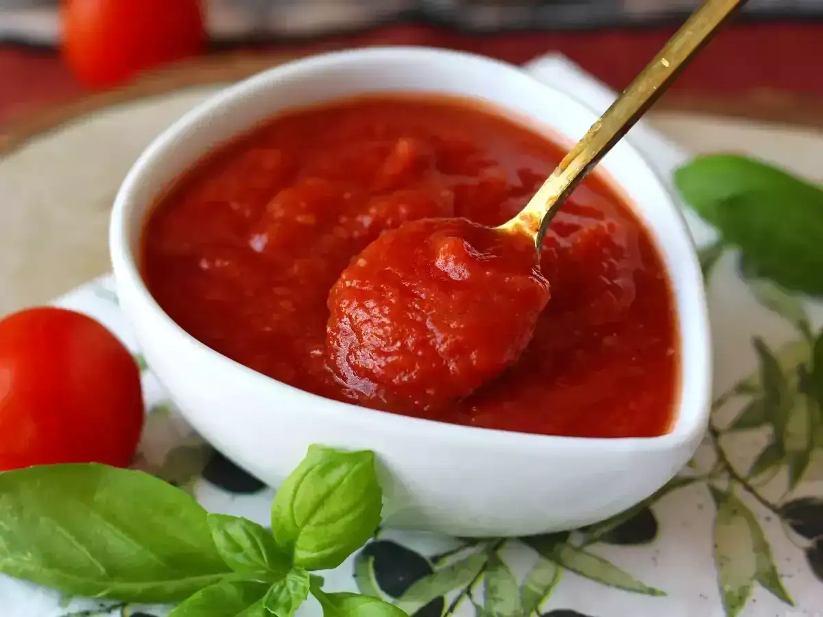 En sked fylld med hemlagad tomats&aring;s, perfekt f&ouml;r pasta italiano. Tomater och basilika i n&auml;rheten.