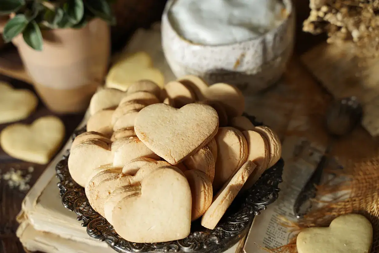 Stos serduszkowych ciastek bez glutenu na ozdobnej tacy, obok książek i rośliny.