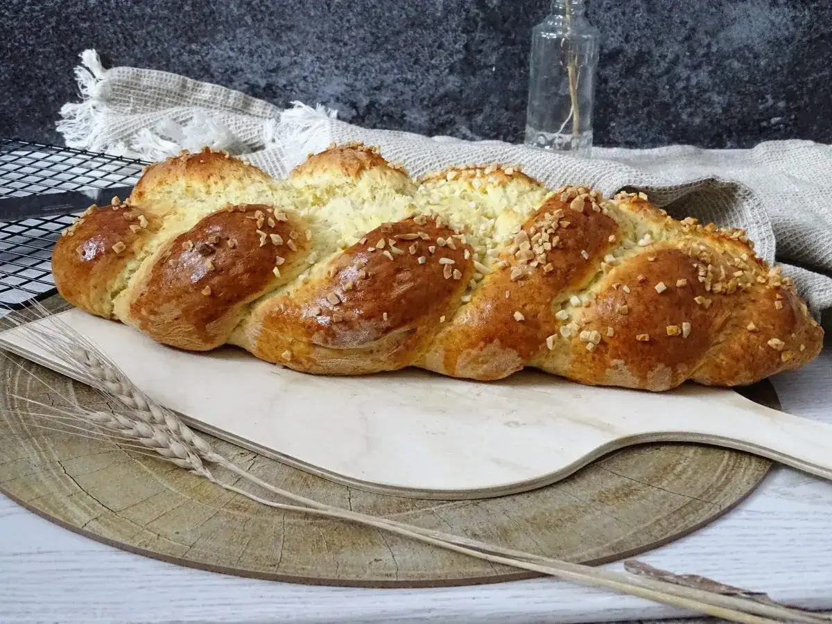 Goldbrauner Osterzopf mit Quark, bestreut mit gehackten N&uuml;ssen, liegt auf einem Holzbrett.