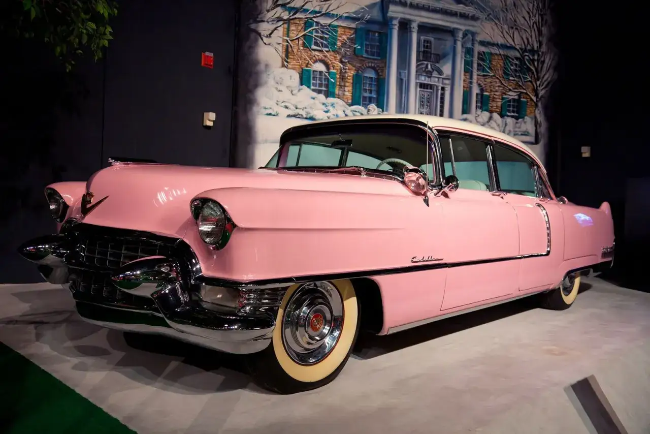 Ein rosafarbener Cadillac, ein ikonisches Elvis Presley Auto, steht vor einer gemalten Kulisse von Graceland im Schnee.