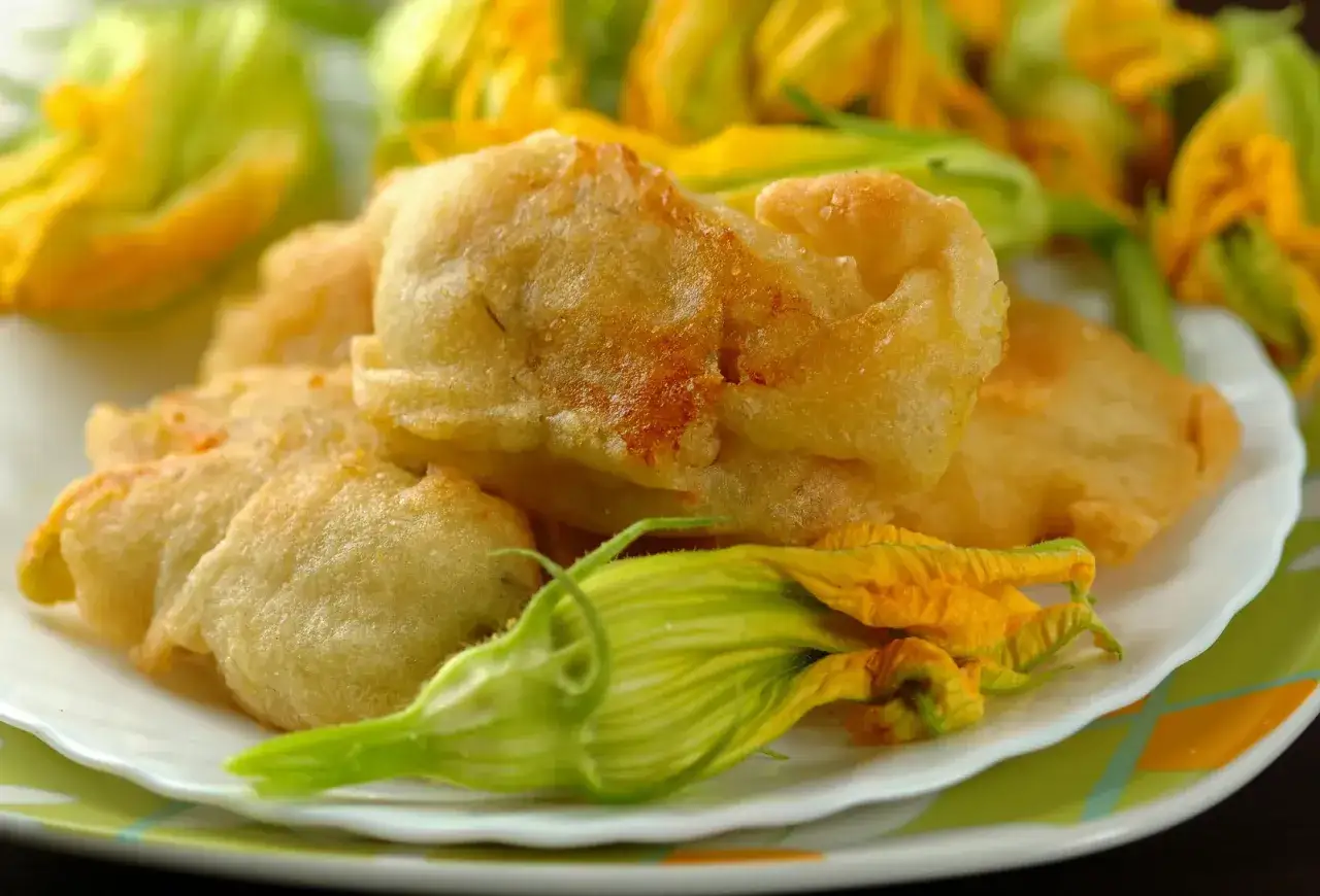 Fiori di zucca in friggitrice ad aria, dorati e croccanti, serviti su un piatto con fiori freschi.