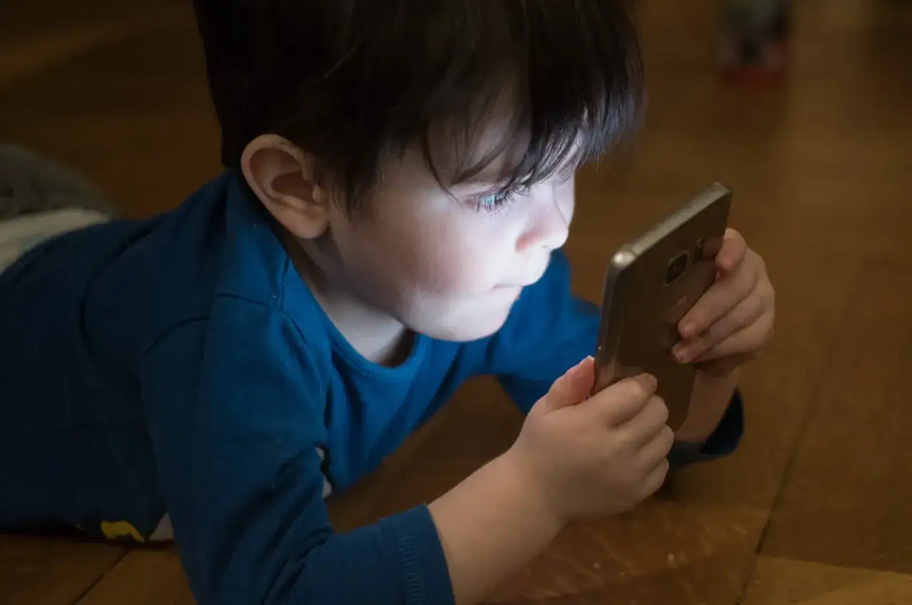 Małe dziecko zafascynowane ekranem telefonu. Rodzice dbają o bezpieczeństwo, stosując blokadę rodzicielską na telefon.