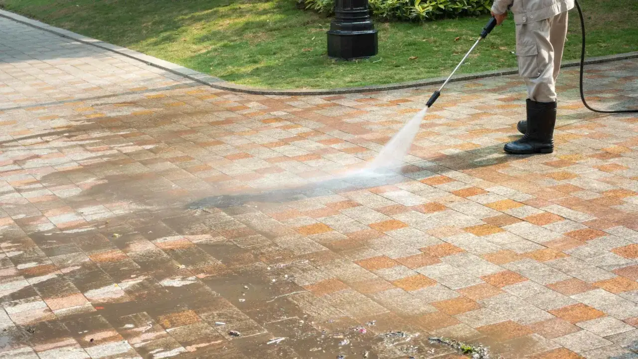 Un homme en bottes nettoie une terrasse en b&eacute;ton avec un nettoyeur haute pression. L'eau projet&eacute;e r&eacute;v&egrave;le la propret&eacute; retrouv&eacute;e.