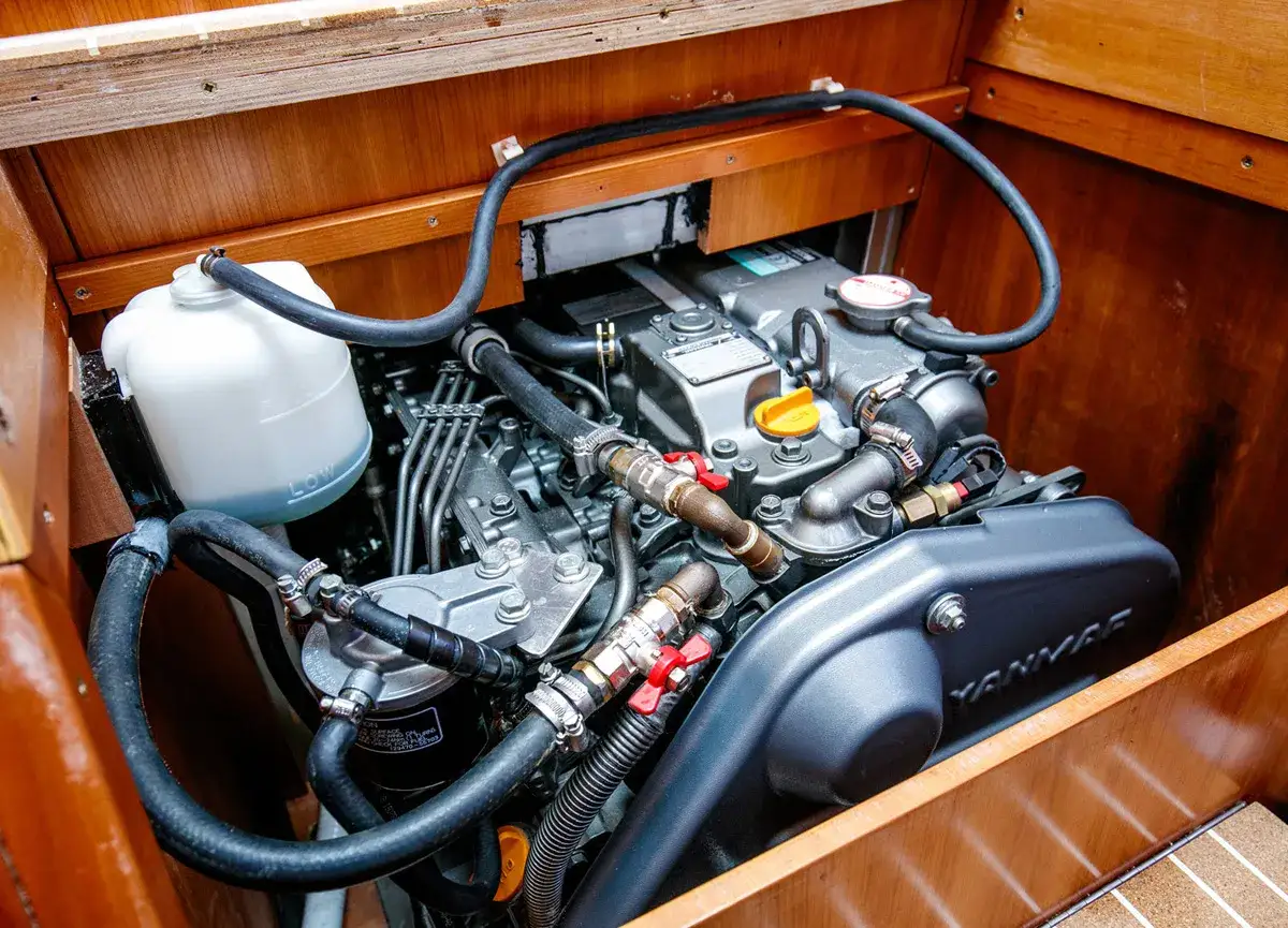 Motore marino Yanmar in vano legnoso, pronto per la manutenzione. Tubi, filtri e serbatoio liquido visibili.