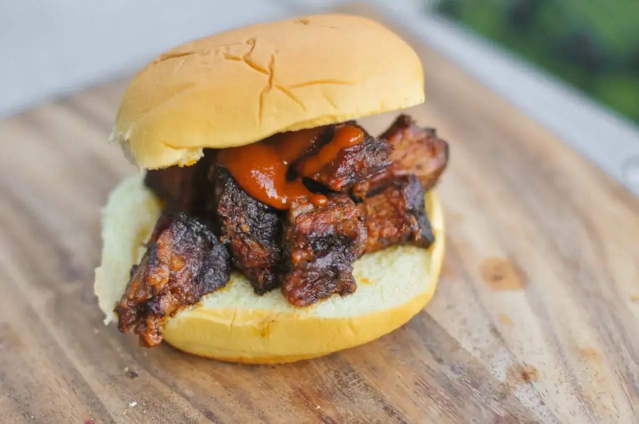 Saftiger Burger mit zarten **burnt ends** und BBQ-Sauce auf einem Holzbrett.