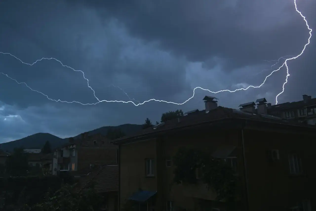 Grzmoty i błyskawice nad miastem, wywołujące fonofobię. Ciemne chmury i rozświetlone niebo nad dachami domów.