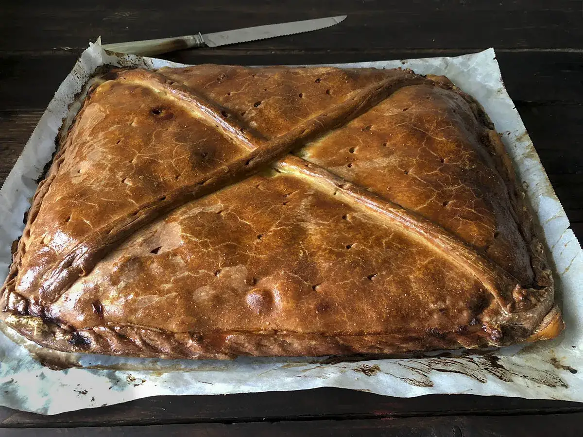 Empanada de atún dorada y crujiente, lista para ser cortada. Su masa presenta un diseño cruzado y bordes trenzados.