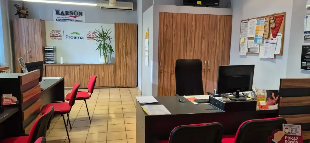 Wnętrze biura ubezpieczeniowego z biurkami, krzesłami i szafkami.