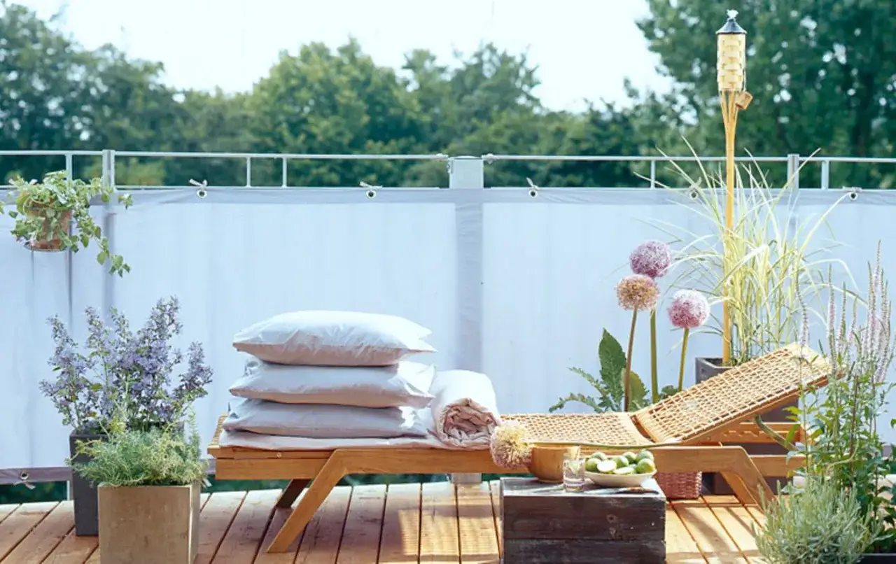 Entspannende Terrasse mit Liege, Kissen und vielen Pflanzen, darunter dekorative Zwiebelblumen. Eine Tiki-Fackel sorgt für Atmosphäre.
