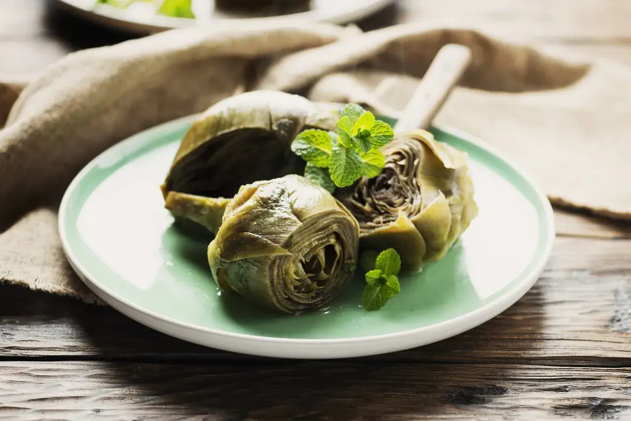 Carciofi alla romana, uno dei 10 piatti tipici del Lazio, serviti su un piatto verde con menta fresca.