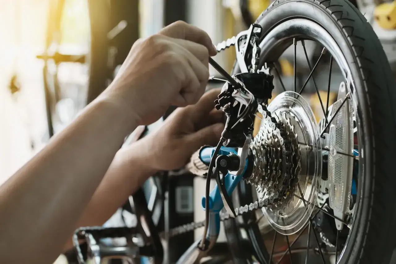 Hands performing a rei bike tune up, adjusting the derailleur and chain on a bicycle's rear wheel.