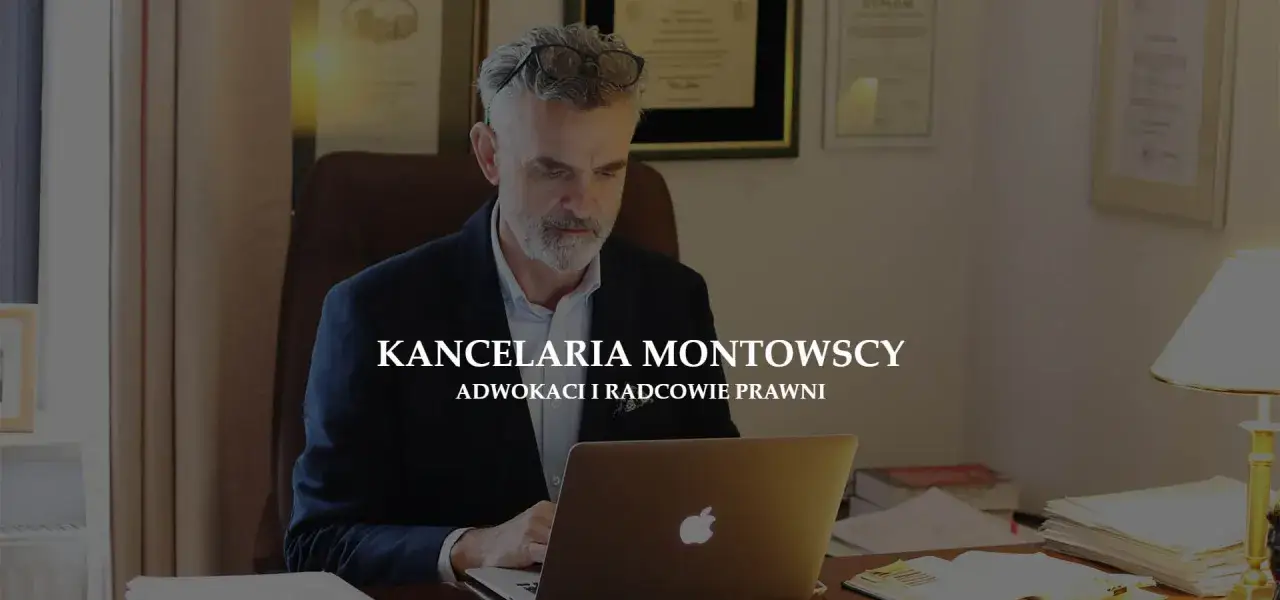 Mężczyzna w okularach siedzi przy biurku z laptopem, na ścianie dyplomy.