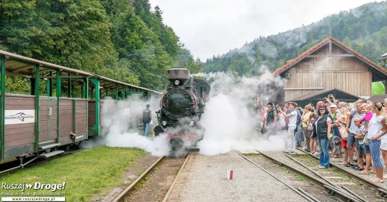 Parowóz Bieszczadzkiej Kolejki Leśnej z parą, tłum ludzi czeka na przejażdżkę. To świetne bieszczady atrakcje dla dzieci.