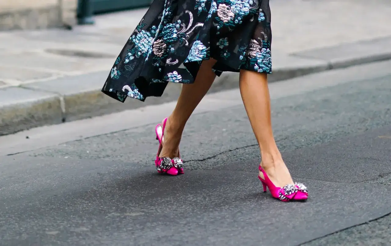 Piernas luciendo un vestido floral negro y zapatos fucsia con lazos brillantes. Un look smart elegant para pasear.