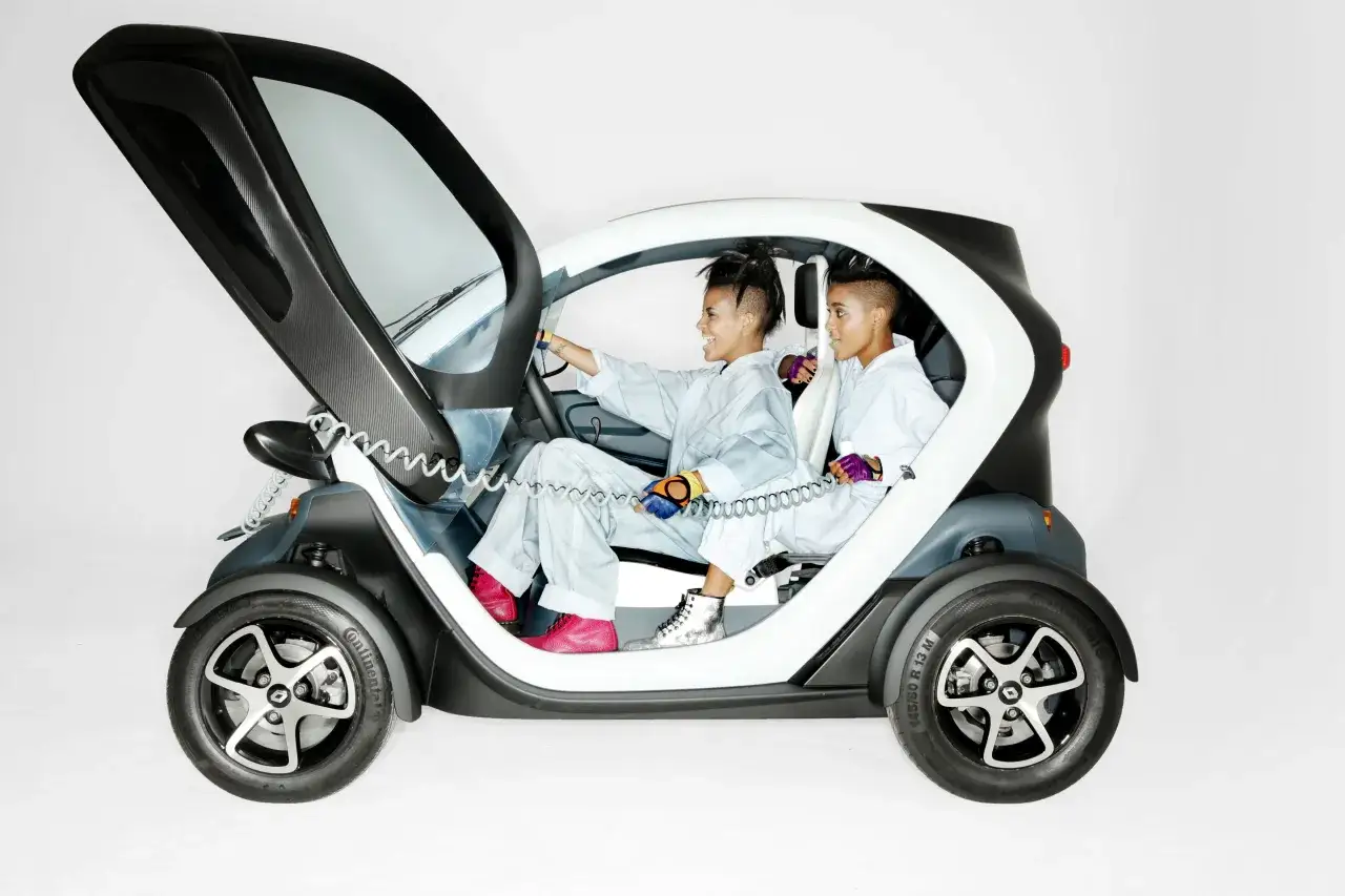 Dwie kobiety w kombinezonach siedzą w Renault Twizy. Jedna z nich kieruje, druga trzyma coś w ręku.