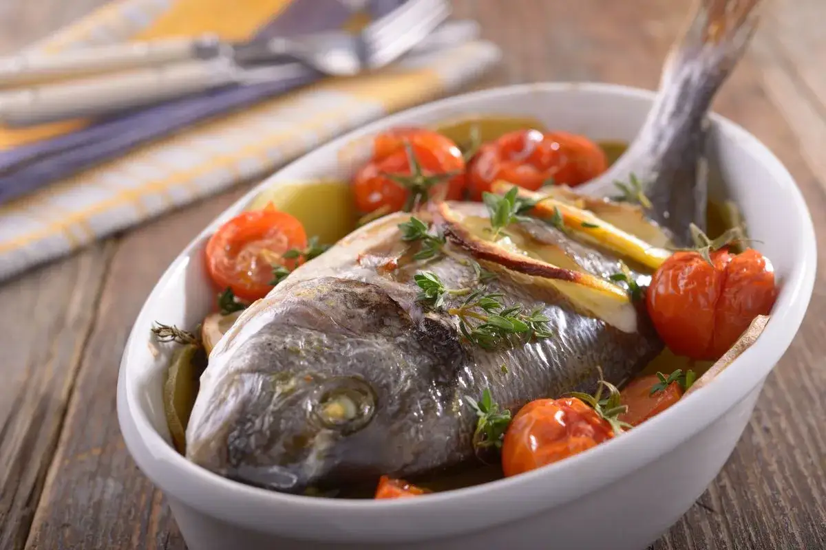 Orata al forno succulenta con pomodorini, limone e erbe aromatiche, pronta per essere gustata.